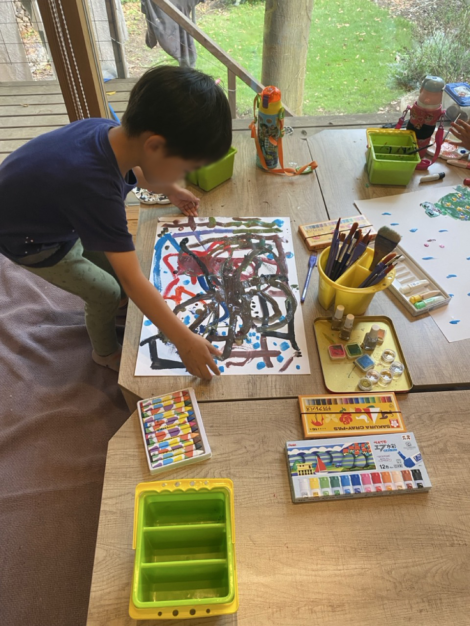大きな紙に絵を描く子どもの手元と画材